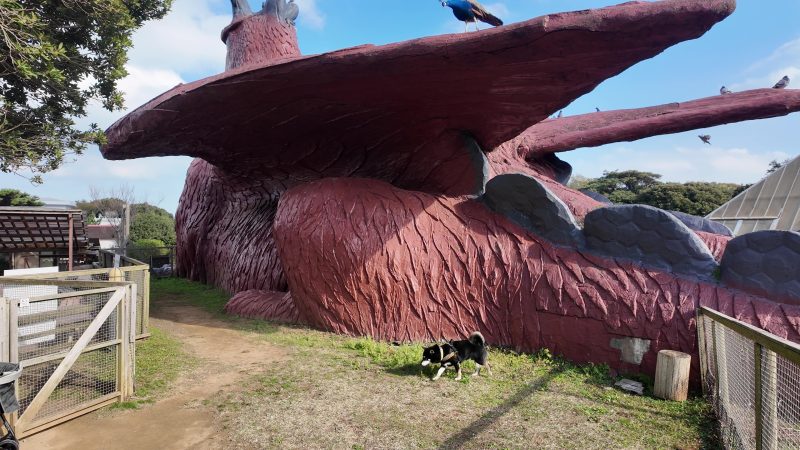 巨大な恐竜の像の前にいる柴犬